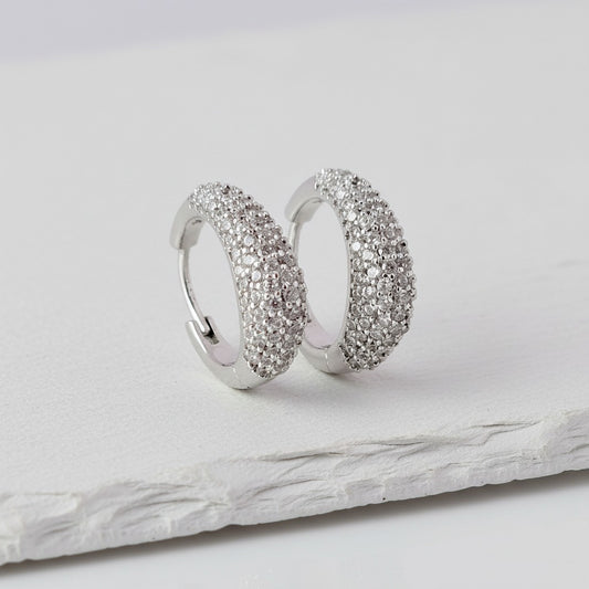Pair of silver hoop earrings with embedded stones on a light gray surface.