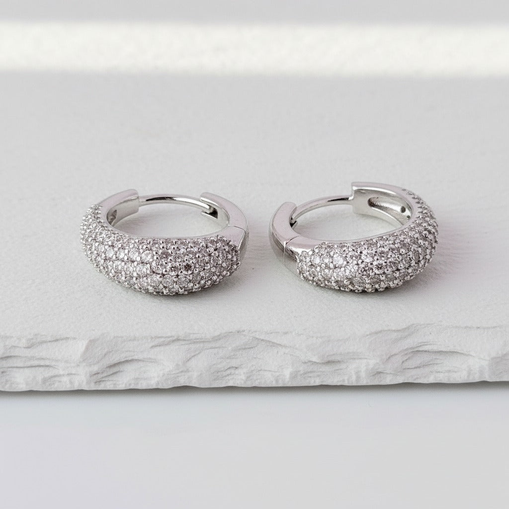 Pair of silver hoop earrings with sparkling stones on a marble surface