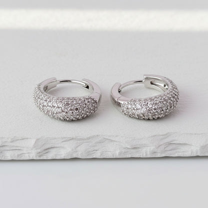 Pair of silver hoop earrings with sparkling stones on a marble surface