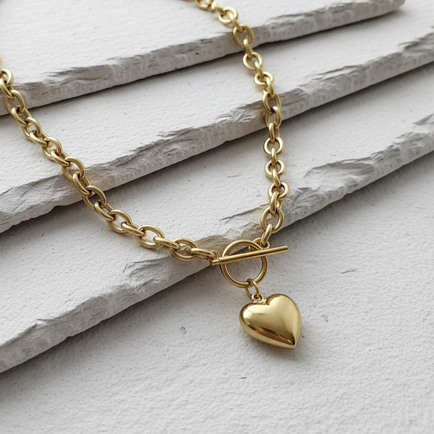 Gold necklace with a heart pendant on a light stone surface