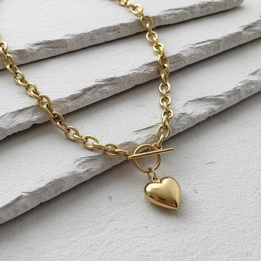 Gold necklace with a heart pendant on a light stone surface