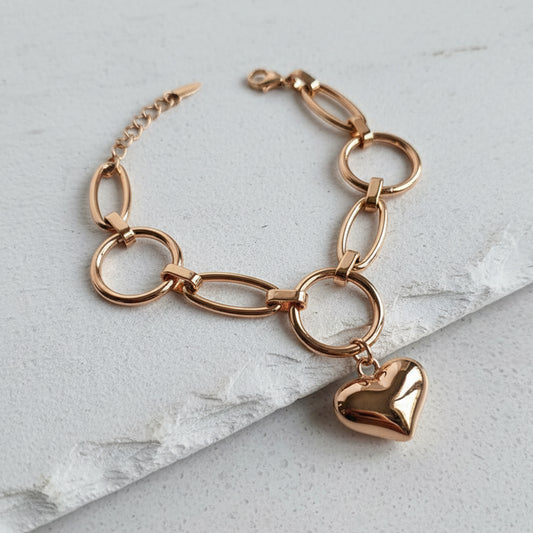 Rose gold bracelet with a heart charm on a light gray marble surface